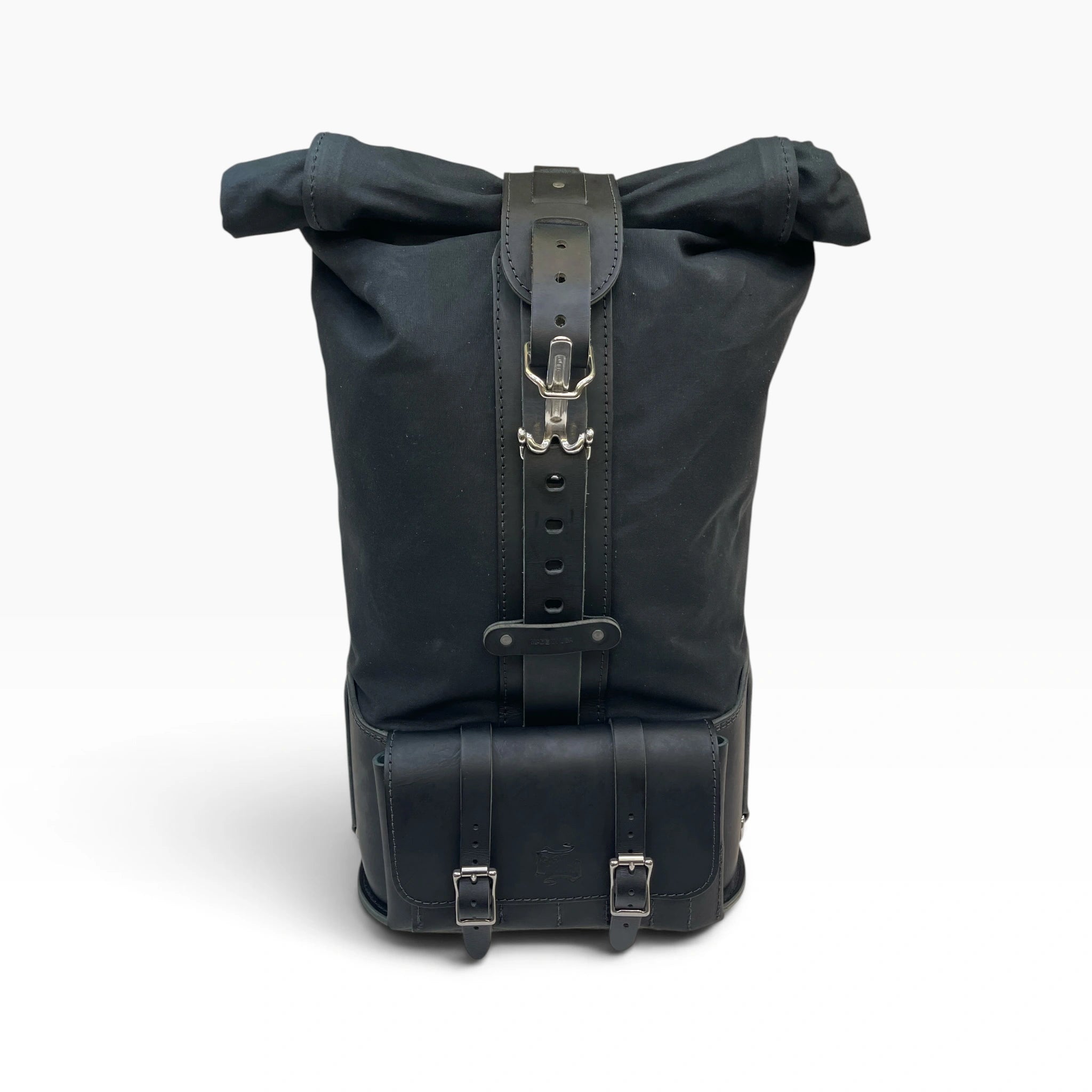 A black roll-top backpack with dark leather straps, buckles, and a front utility pocket, shown against a plain white background.
