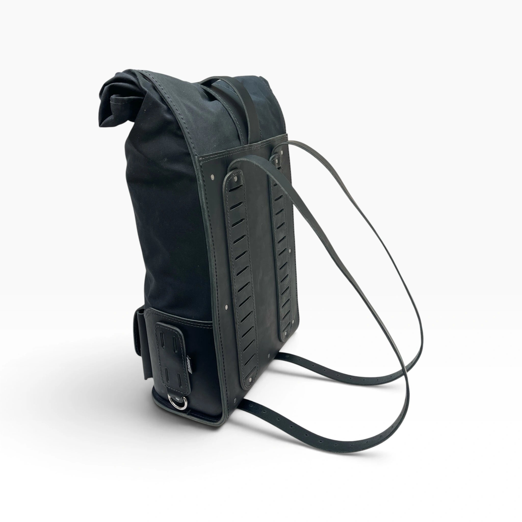 A black roll-top backpack shown from a side angle on a clean white studio background, featuring a long shoulder strap and structured leather-like side panels.