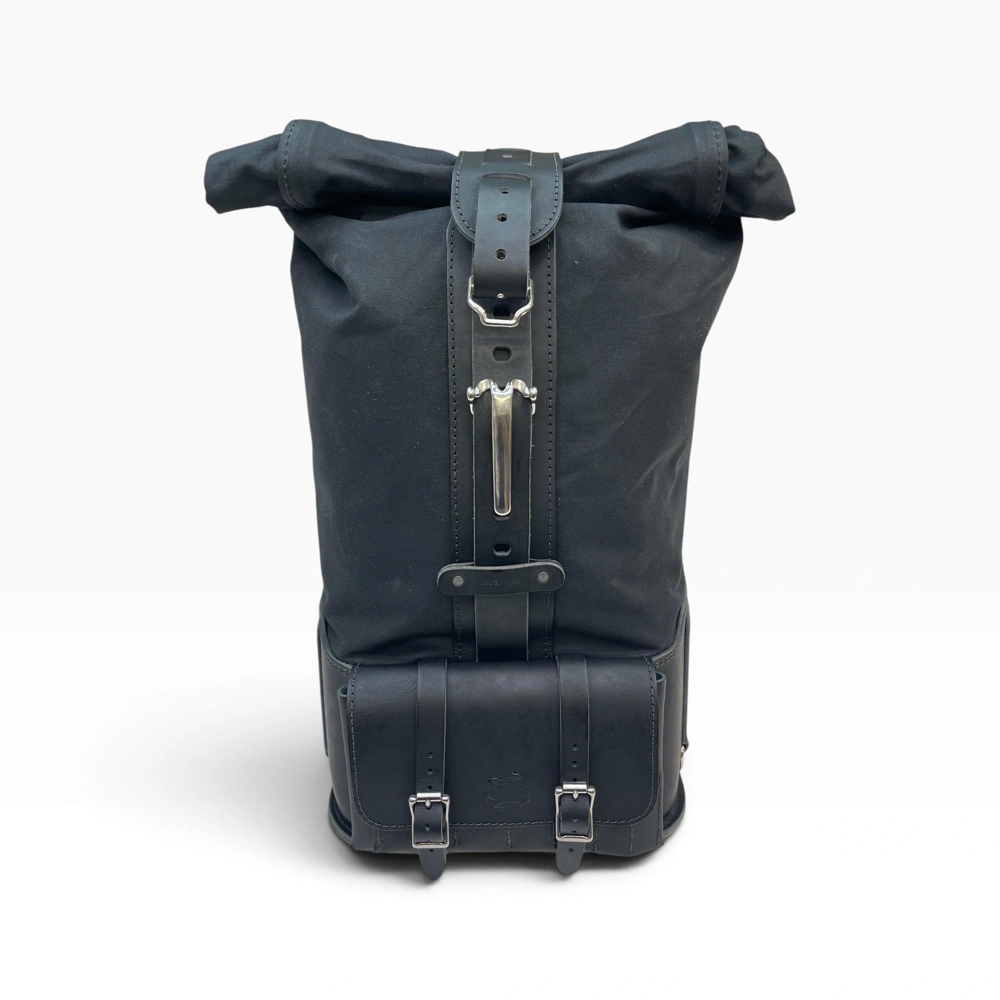 A black roll-top backpack made of durable canvas and leather, featuring silver metal buckles and a vertical strap closure, shown against a plain white background.