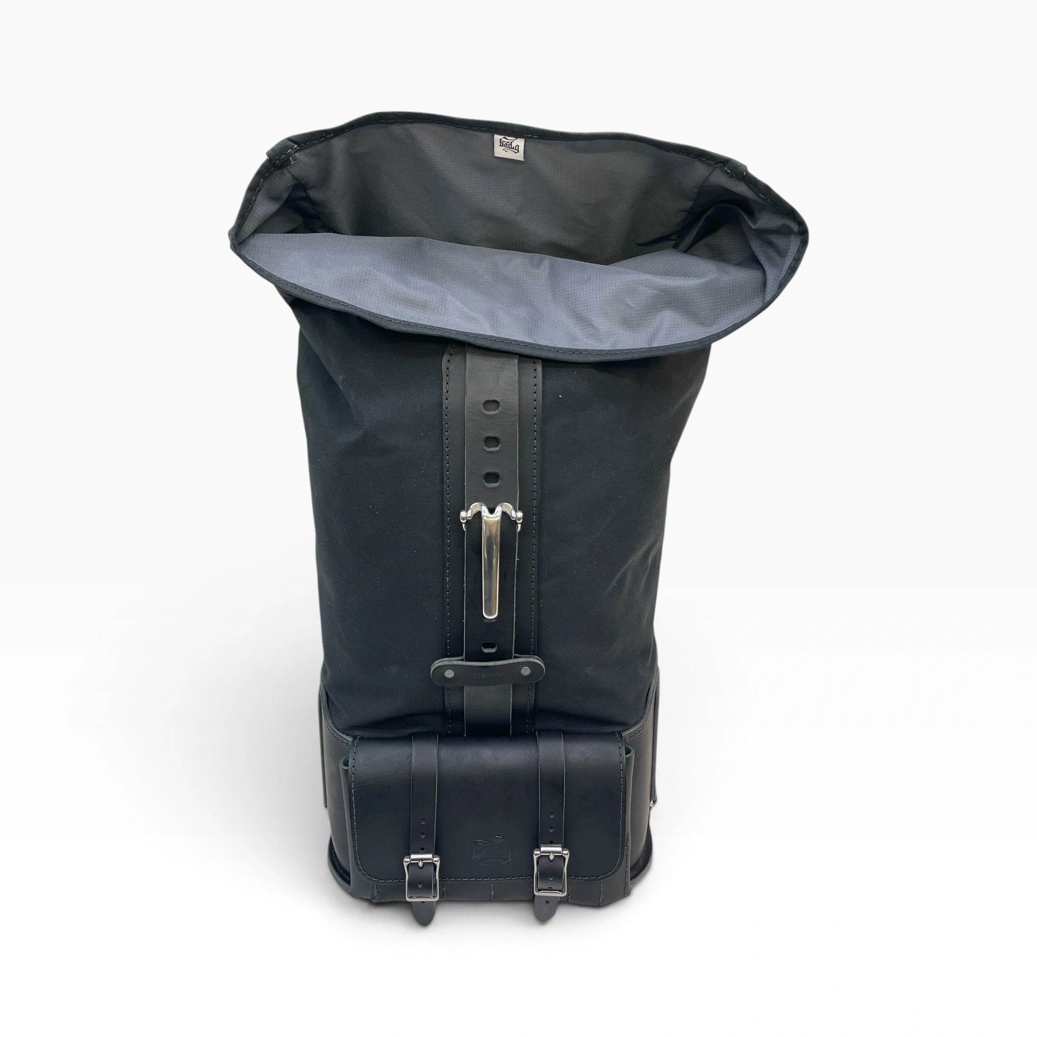 A black roll-top backpack with a gray interior lining, featuring a central strap with a silver metal buckle and a lower buckle-secured base, shown on a white background.