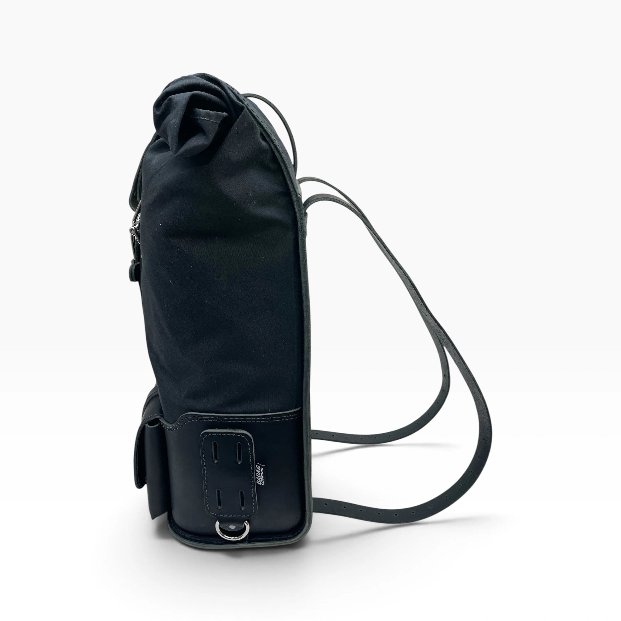 A black canvas backpack shown from the side profile on a clean white background, featuring a long shoulder strap and a bottom buckle closure.